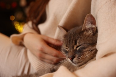 Photo of Woman with cute cat against blurred Christmas lights, closeup