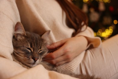 Photo of Woman with cute cat against blurred Christmas lights, closeup