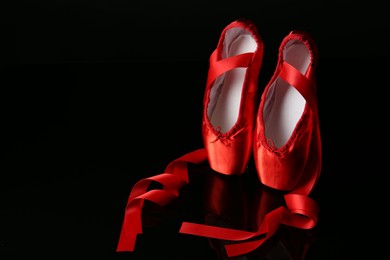 Photo of Pair of beautiful pointe shoes on black mirror surface. Space for text