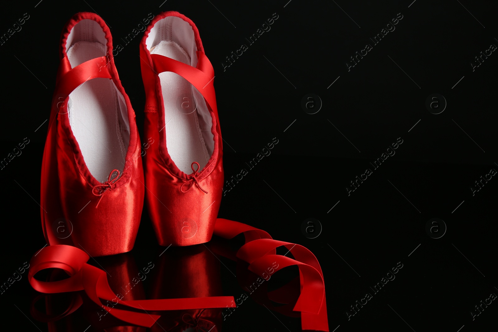 Photo of Pair of beautiful pointe shoes on black mirror surface. Space for text