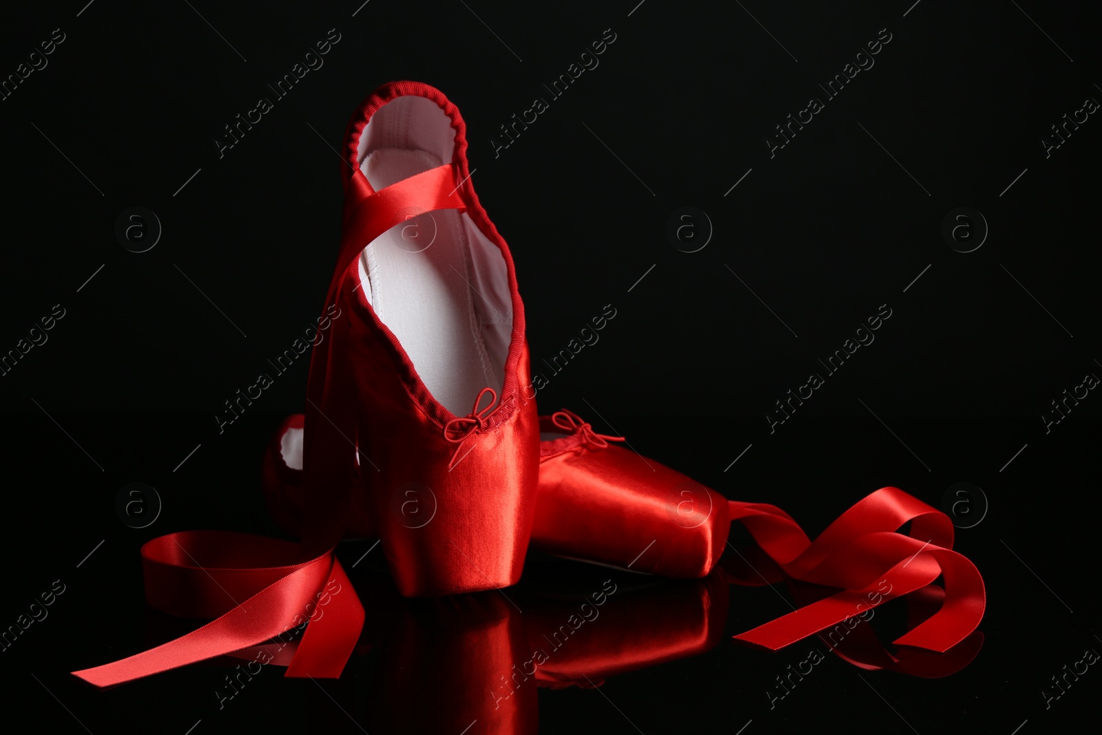 Photo of Pair of beautiful pointe shoes on black mirror surface