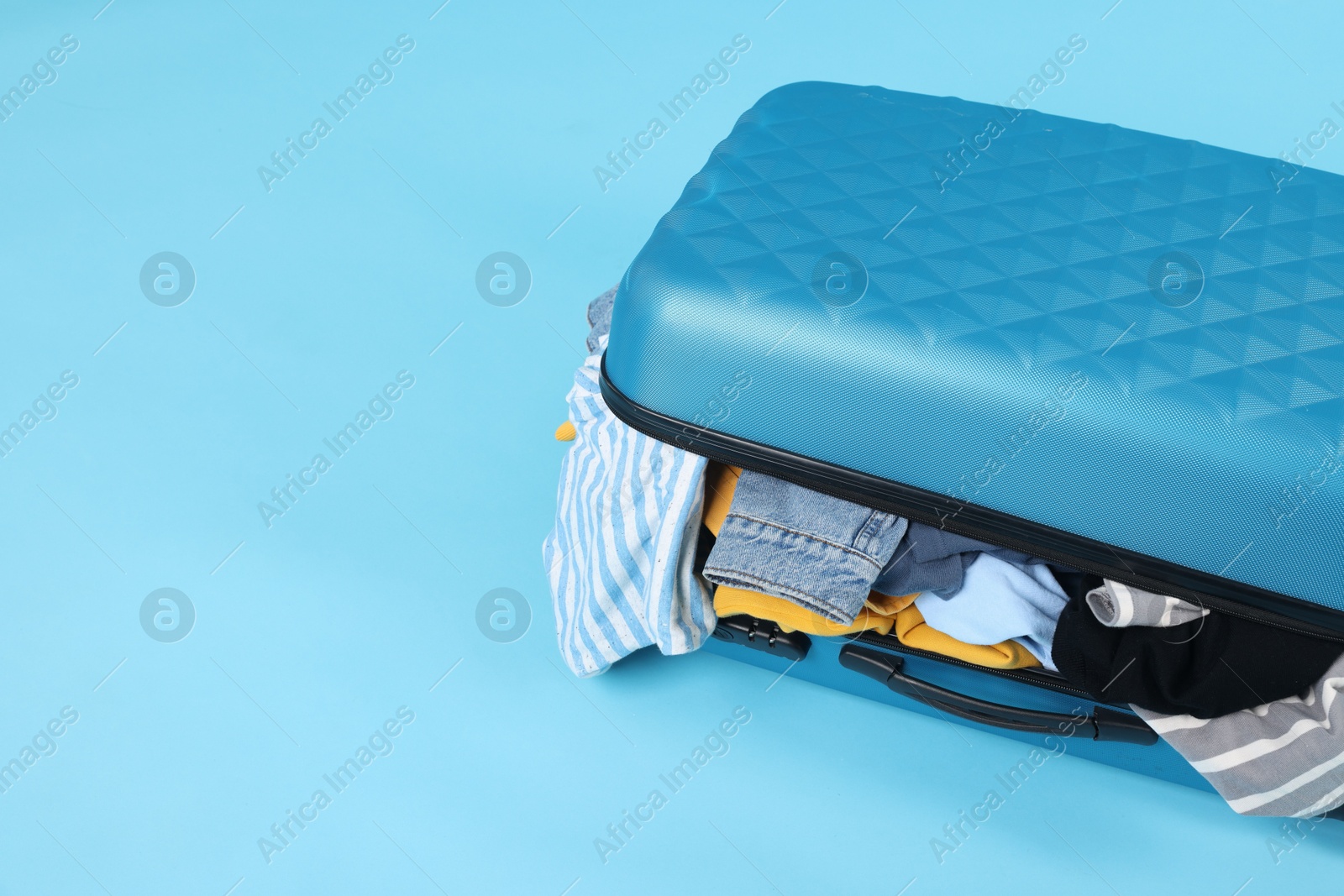 Photo of Packed suitcase full of clothes on light blue background, closeup. Space for text