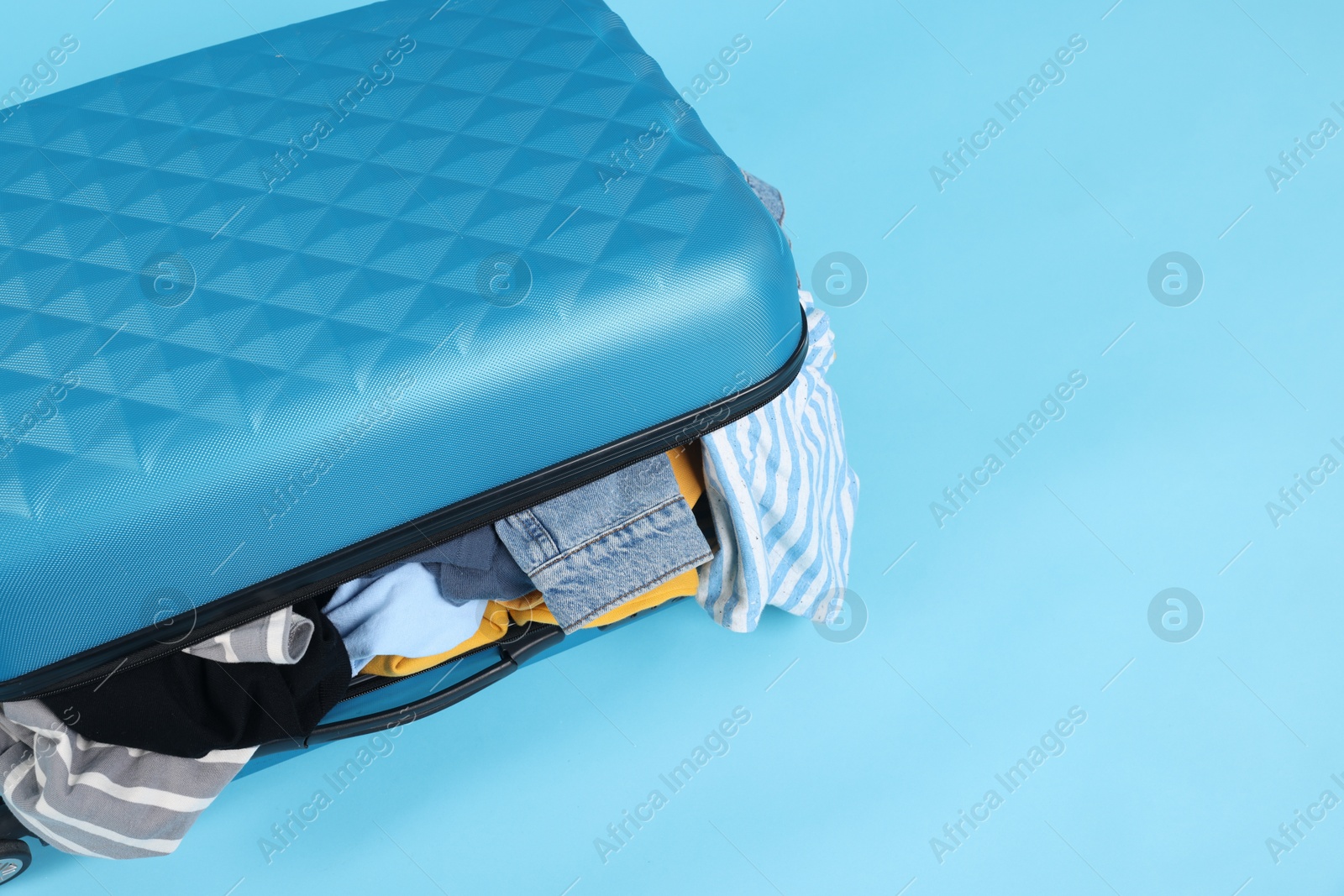 Photo of Packed suitcase full of clothes on light blue background, closeup. Space for text