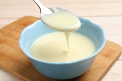 Photo of Condensed milk flowing down from spoon into bowl on wooden table, closeup