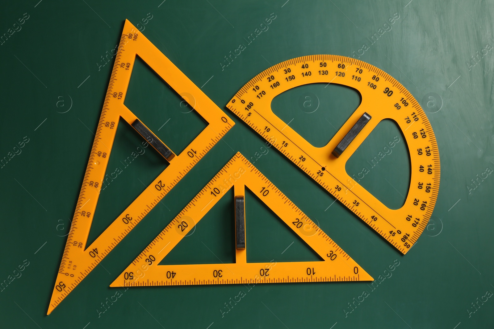 Photo of Protractor and triangle rulers on green chalkboard, flat lay