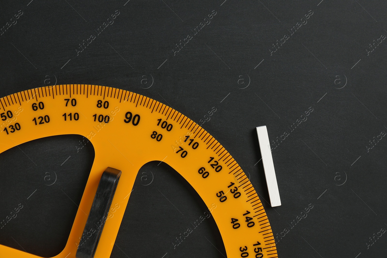 Photo of Protractor ruler and chalk on black chalkboard, top view. Space for text