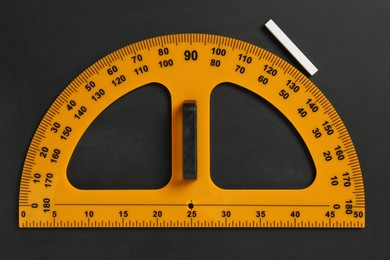 Photo of Protractor ruler and chalk on black chalkboard, top view