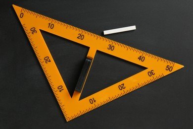 Photo of Triangle ruler and chalk on black chalkboard, top view