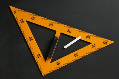 Photo of Triangle ruler and chalk on black chalkboard, top view