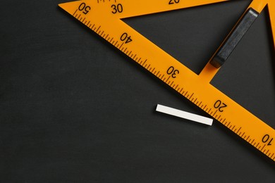 Photo of Triangle ruler and chalk on black chalkboard, top view. Space for text