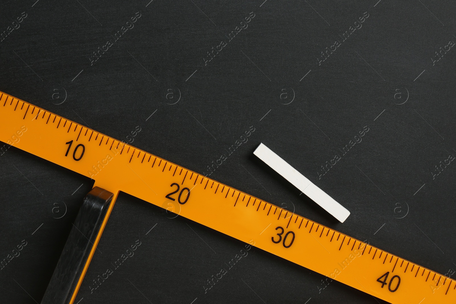 Photo of Triangle ruler and chalk on black chalkboard, top view. Space for text