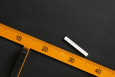 Photo of Triangle ruler and chalk on black chalkboard, top view. Space for text