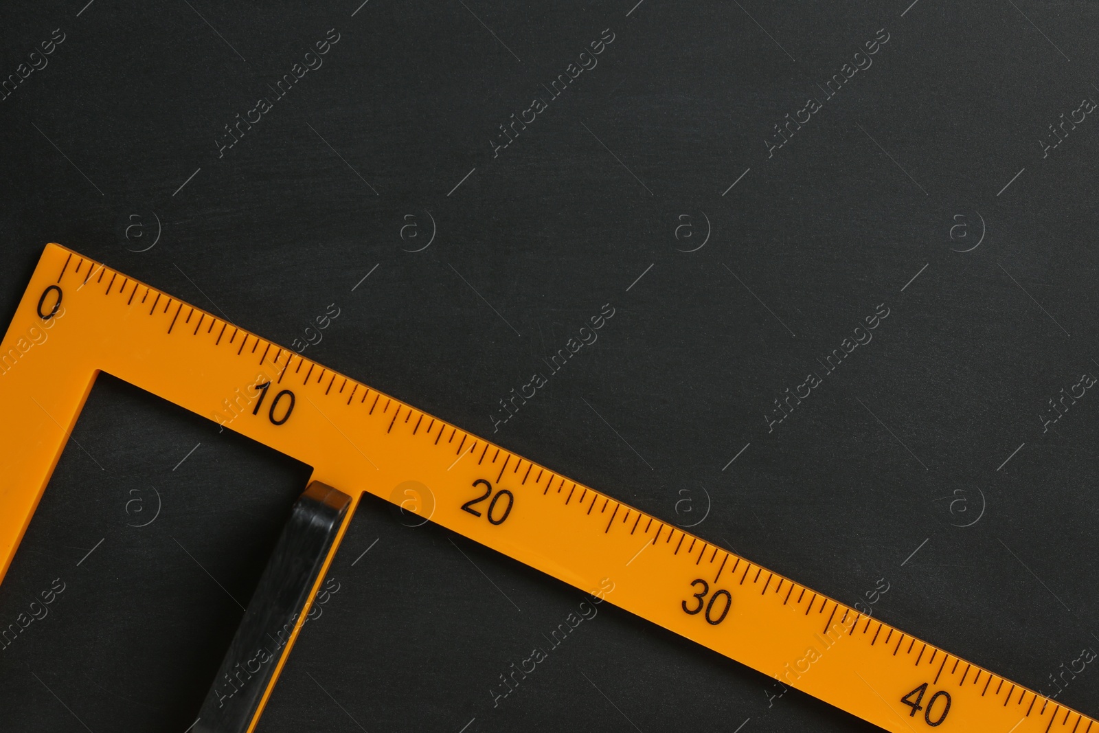 Photo of Triangle ruler on black chalkboard, top view. Space for text