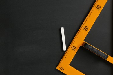 Photo of Triangle ruler and chalk on black chalkboard, top view. Space for text