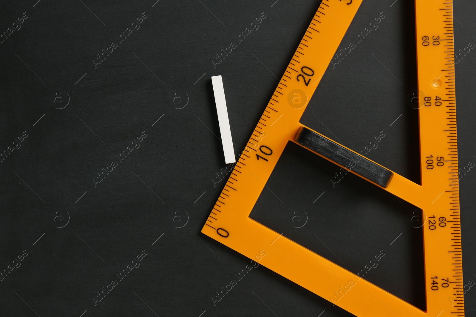 Photo of Triangle ruler and chalk on black chalkboard, top view. Space for text