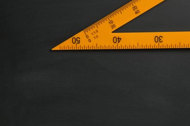 Photo of Triangle ruler on black chalkboard, top view. Space for text