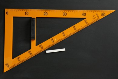 Photo of Triangle ruler and chalk on black chalkboard, top view. Space for text