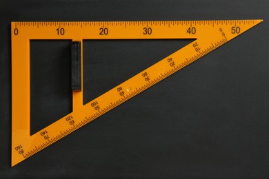 Photo of Triangle ruler on black chalkboard, top view. Space for text