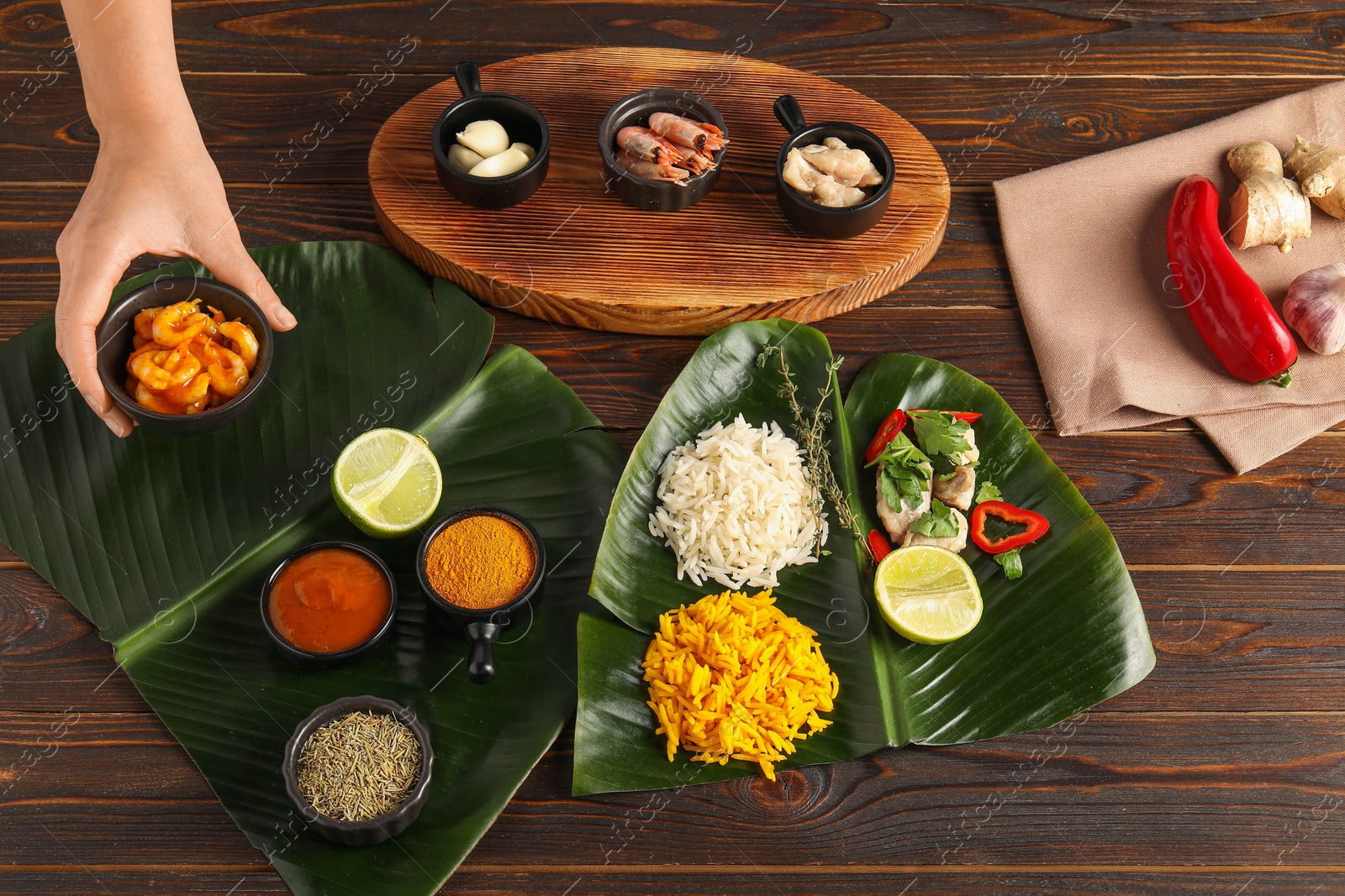 Photo of Woman setting table with cut banana leaves, different food, spices and sauce, top view