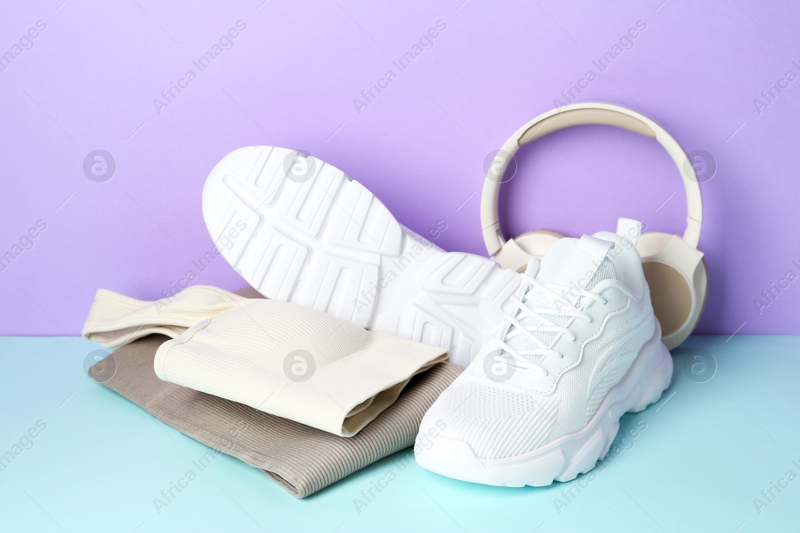 Photo of Pair of stylish white sneakers, sportswear and headphones on color background