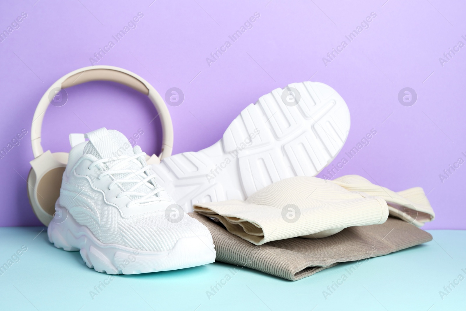 Photo of Pair of stylish white sneakers, sportswear and headphones on color background