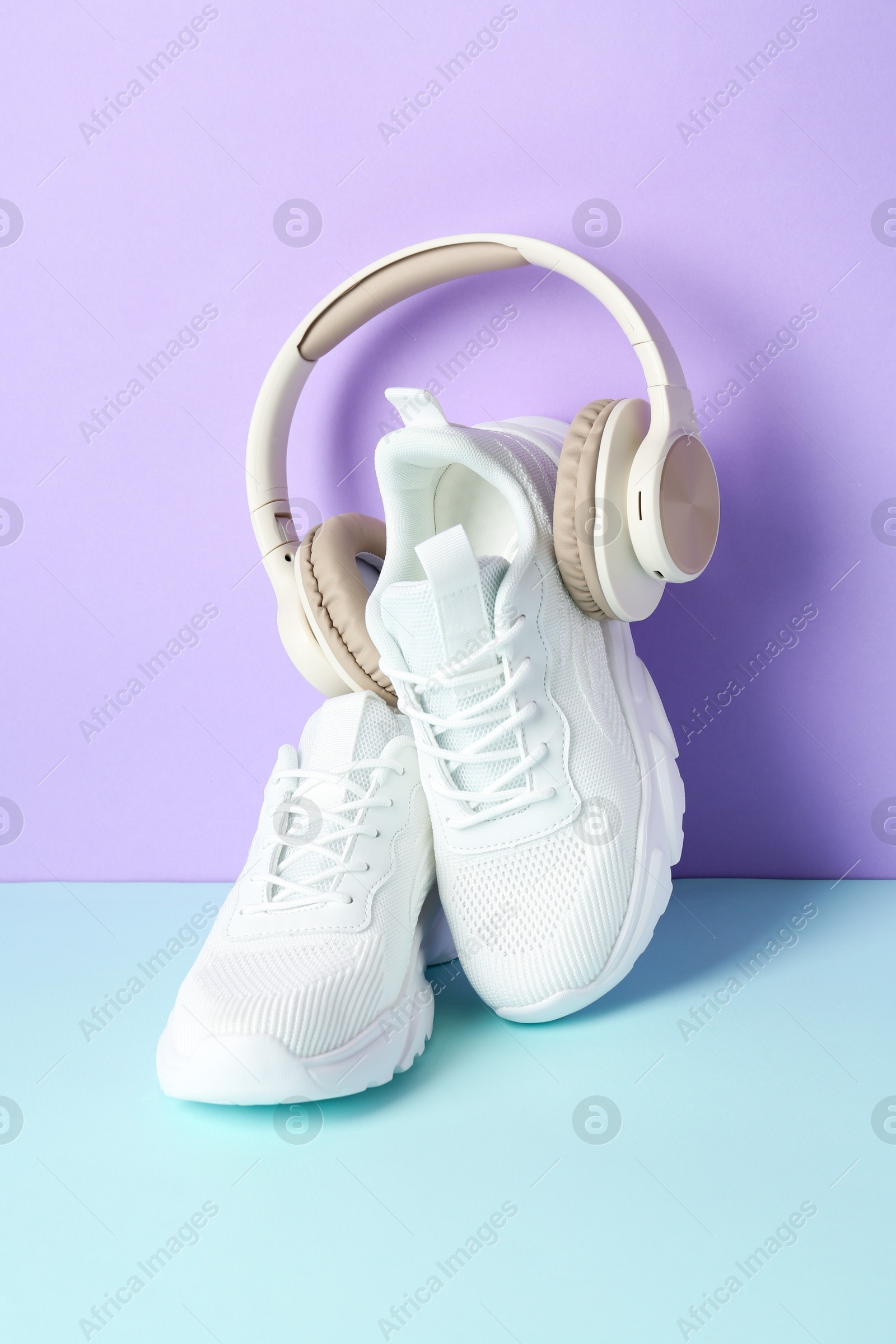 Photo of Pair of stylish white sneakers and headphones on color background