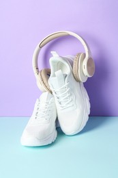 Photo of Pair of stylish white sneakers and headphones on color background