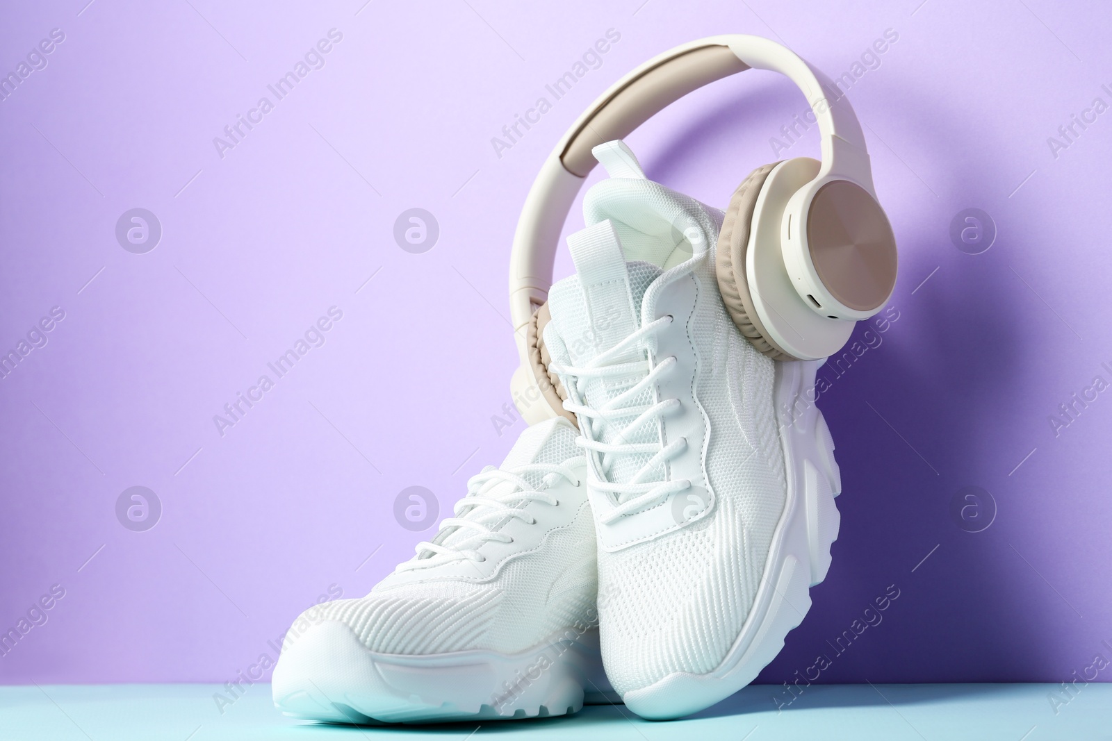 Photo of Pair of stylish white sneakers and headphones on color background