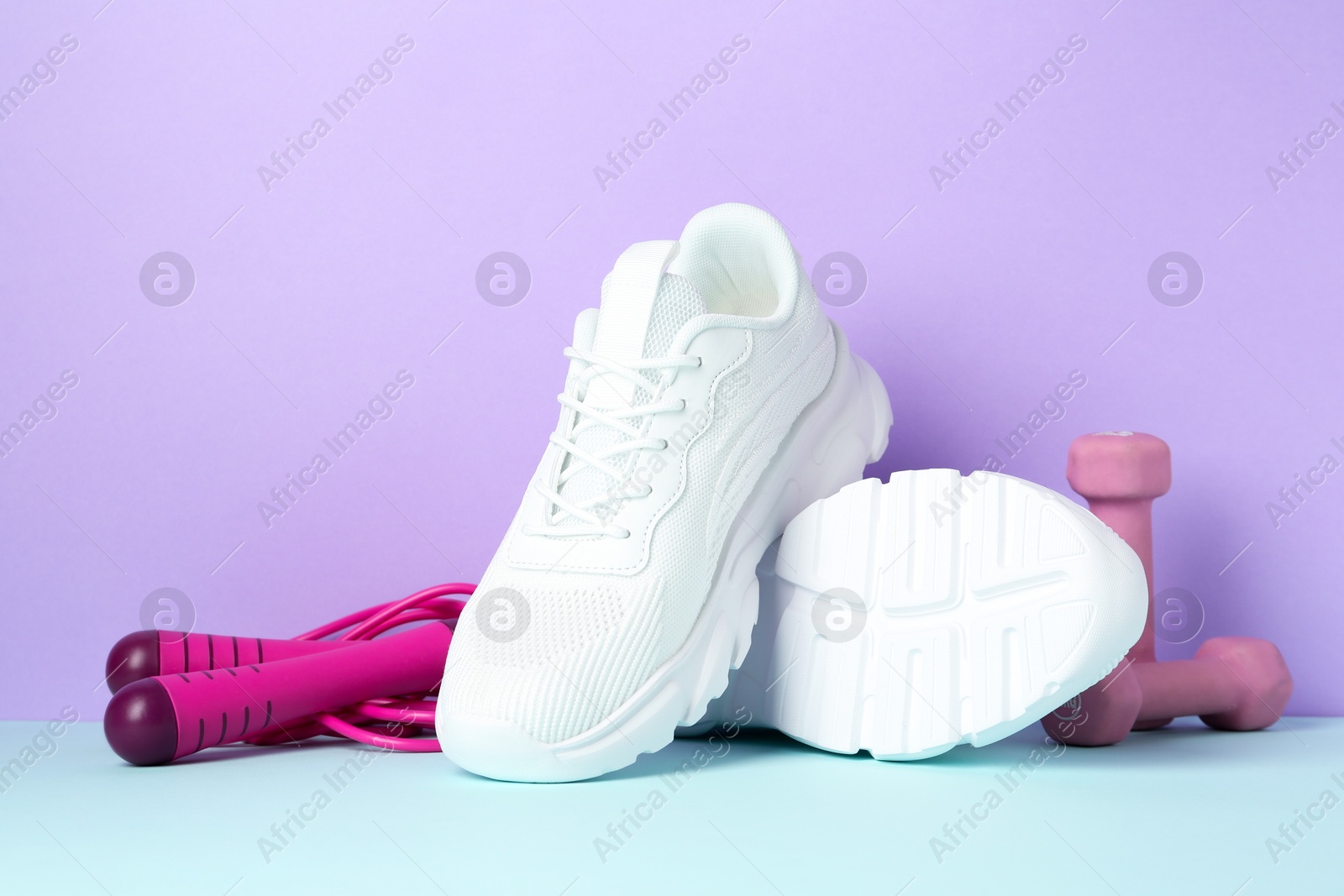 Photo of Pair of stylish white sneakers, dumbbells and skipping rope on color background