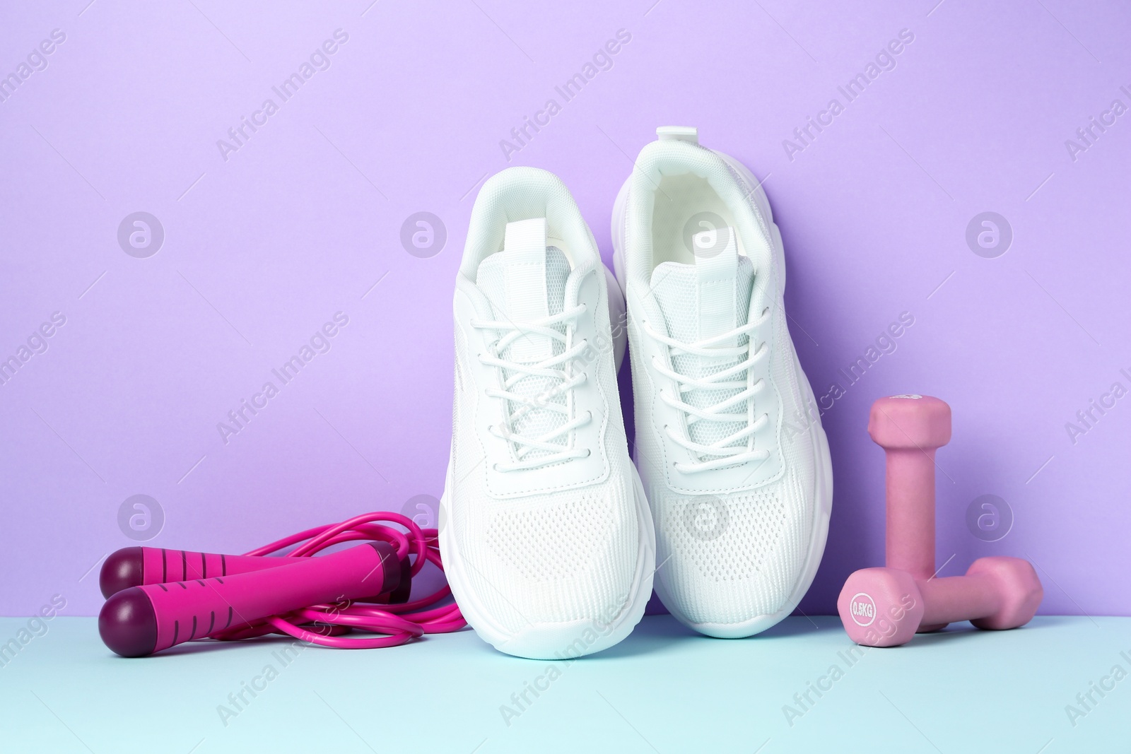 Photo of Pair of stylish white sneakers, dumbbells and skipping rope on color background