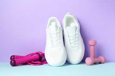 Photo of Pair of stylish white sneakers, dumbbells and skipping rope on color background