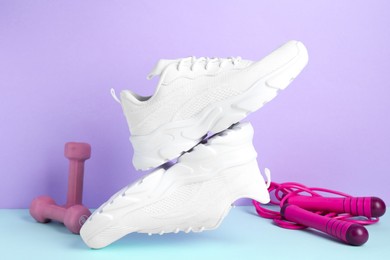 Photo of Pair of stylish white sneakers, dumbbells and skipping rope on color background