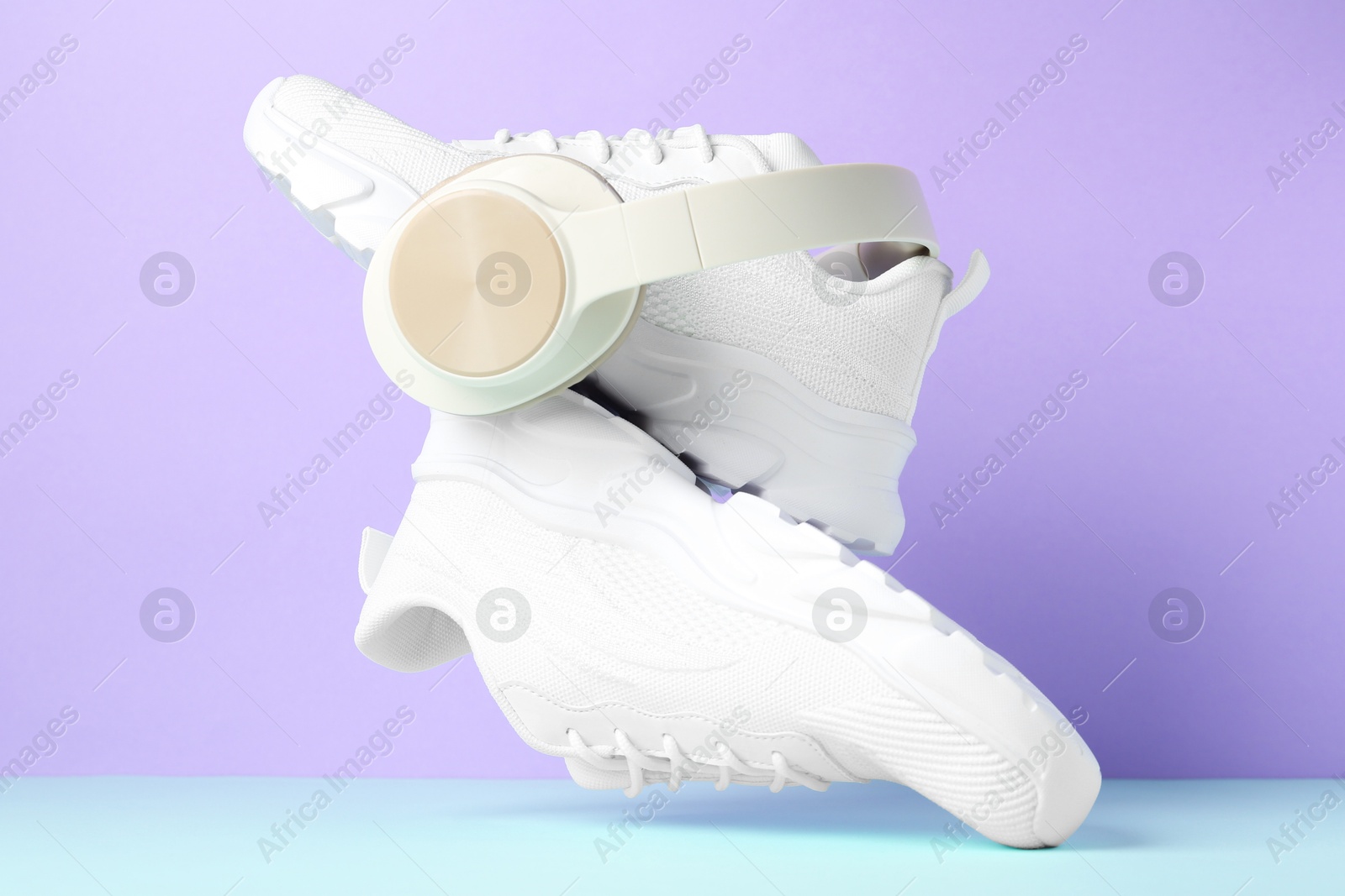 Photo of Pair of stylish white sneakers in air against color background