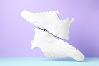 Photo of Pair of stylish white sneakers in air against color background