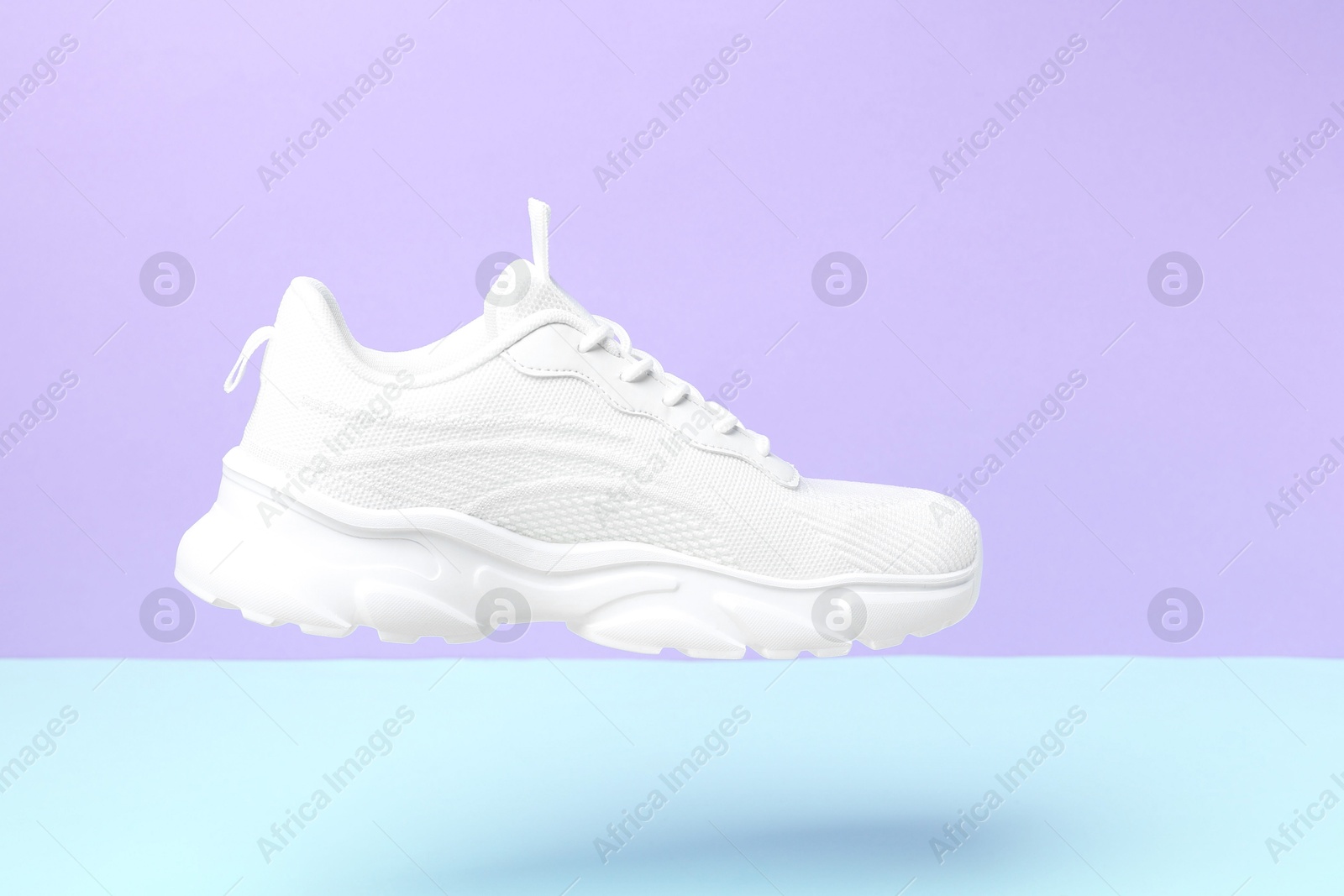 Photo of Stylish white sneaker in air against color background