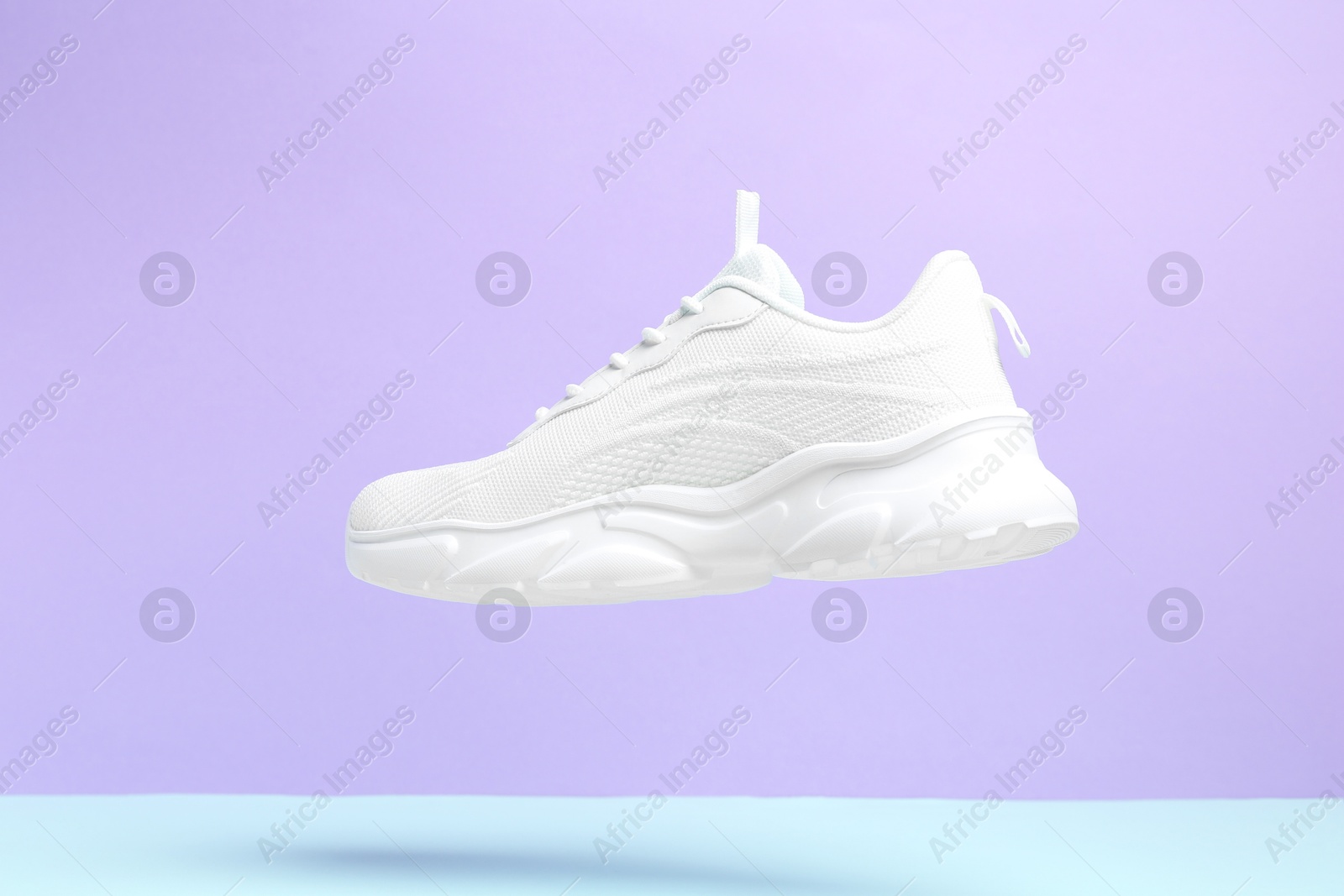 Photo of Stylish white sneaker in air against color background