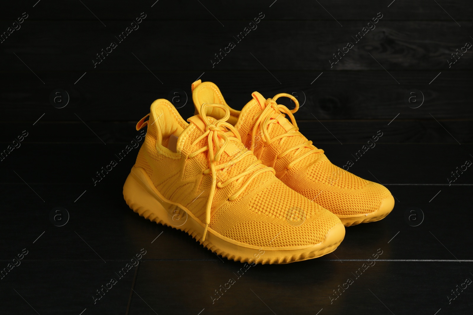 Photo of Pair of stylish yellow sneakers on black wooden background