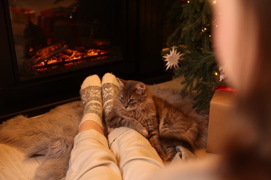 Woman and cute fluffy cat near fireplace in room decorated for Christmas, closeup