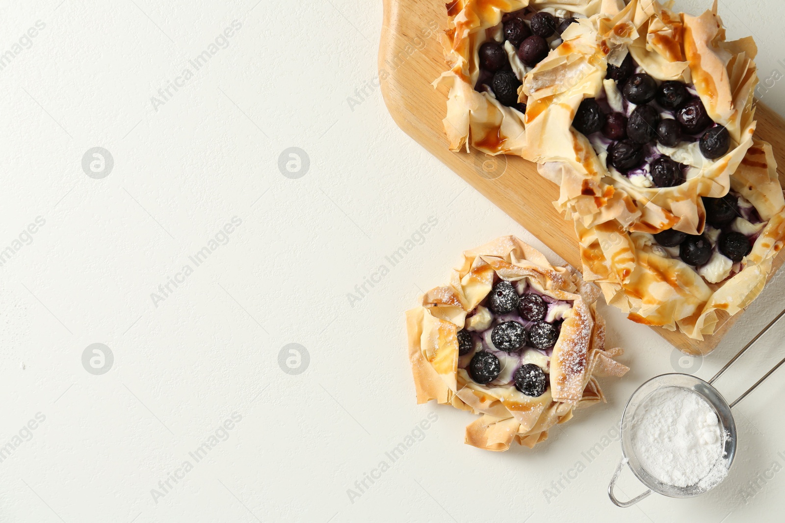 Photo of Delicious puff pastries with blueberries and powdered sugar on white table, flat lay. Space for text