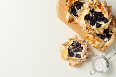 Photo of Delicious puff pastries with blueberries and powdered sugar on white table, flat lay. Space for text