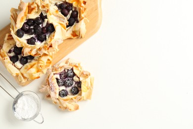 Photo of Delicious puff pastries with blueberries and powdered sugar on white table, flat lay. Space for text