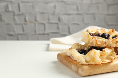 Photo of Delicious puff pastries with blueberries on white table indoors, space for text