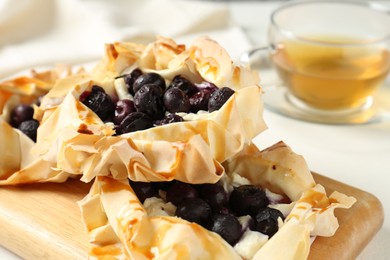 Photo of Delicious puff pastries with blueberries and tea on white table, closeup