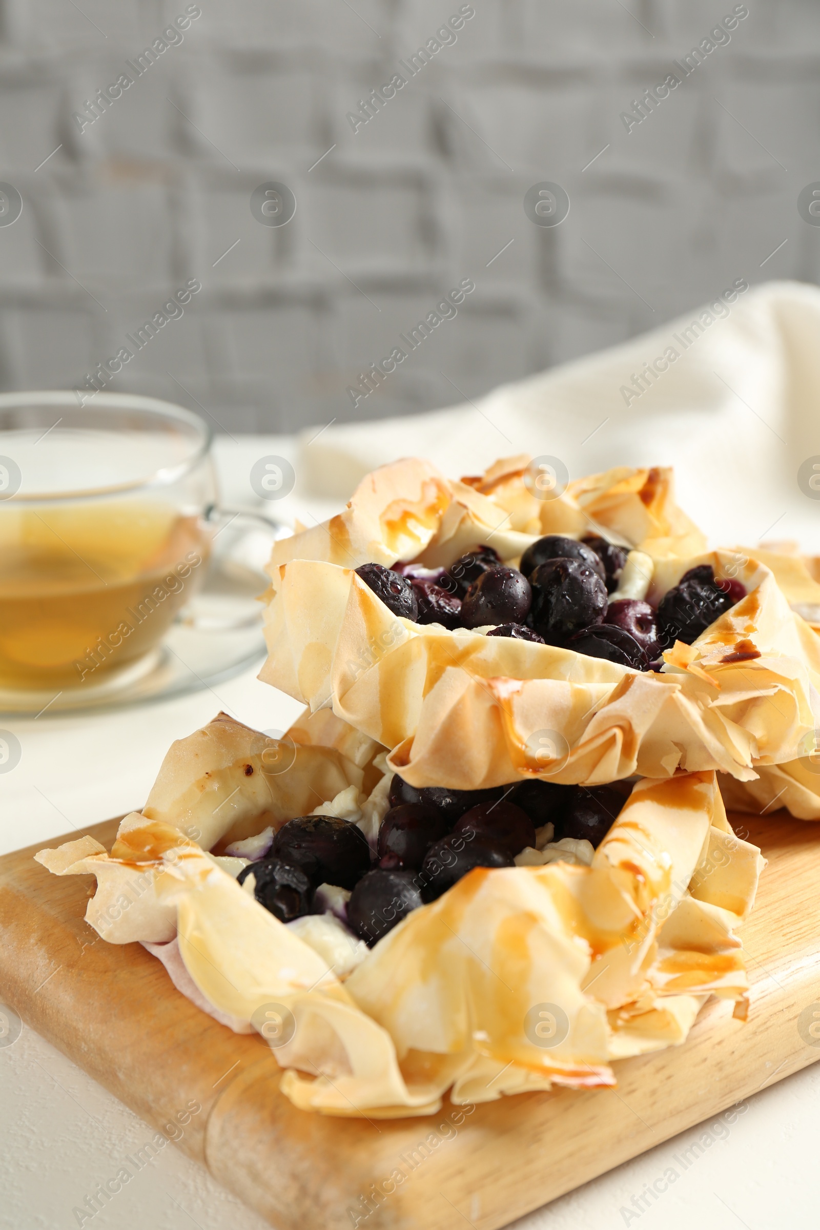 Photo of Delicious puff pastries with blueberries and tea on white table indoors, closeup