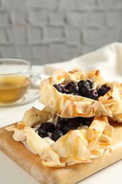 Photo of Delicious puff pastries with blueberries and tea on white table indoors, closeup