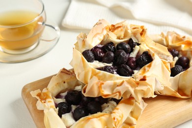 Photo of Delicious puff pastries with blueberries and tea on white table, closeup