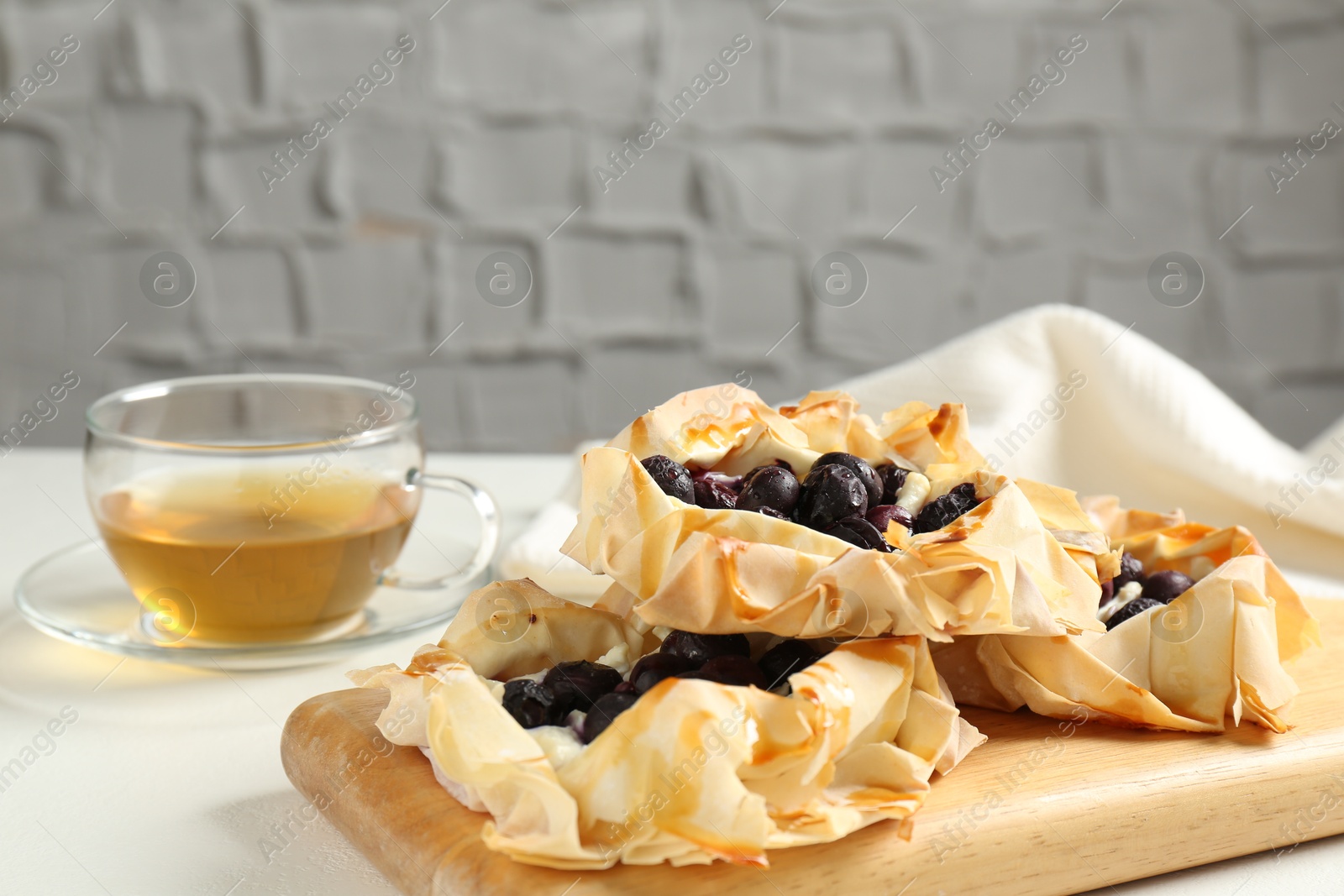 Photo of Delicious puff pastries with blueberries and tea on white table indoors