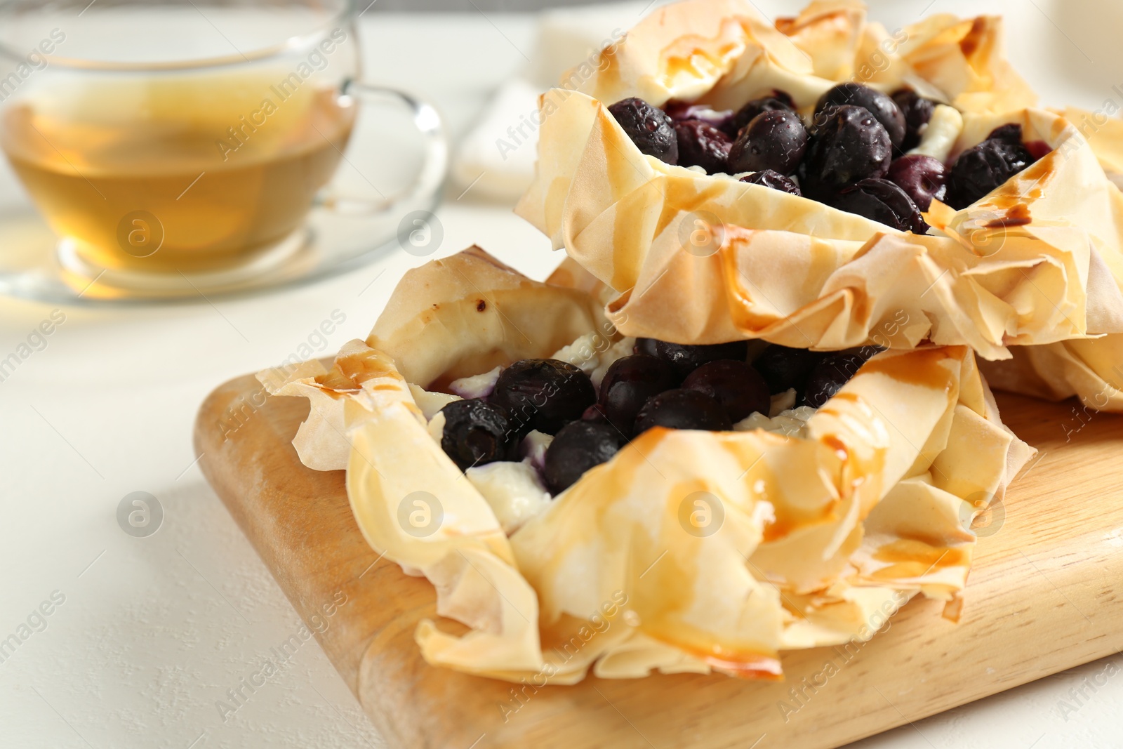 Photo of Delicious puff pastries with blueberries and tea on white table, closeup