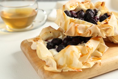 Photo of Delicious puff pastries with blueberries and tea on white table, closeup