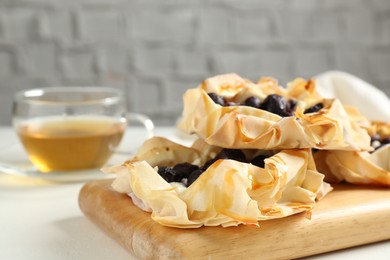 Photo of Delicious puff pastries with blueberries and tea on white table, closeup